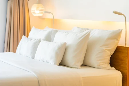 Layered white pillows on a bed with warm ambient lighting.