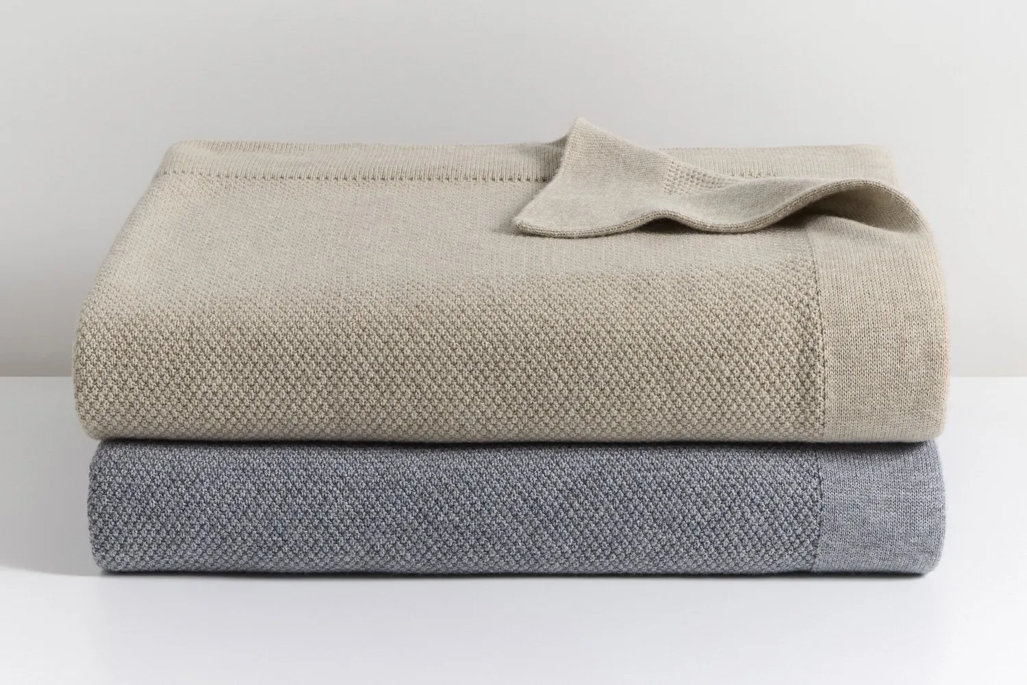 Stacked merino wool blankets in neutral tones showing soft texture and refined knit detail.