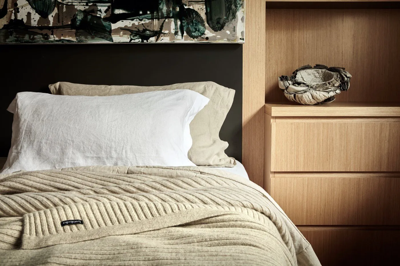 Neutral bedroom setting with a ribbed wool throw layered over linen bedding.