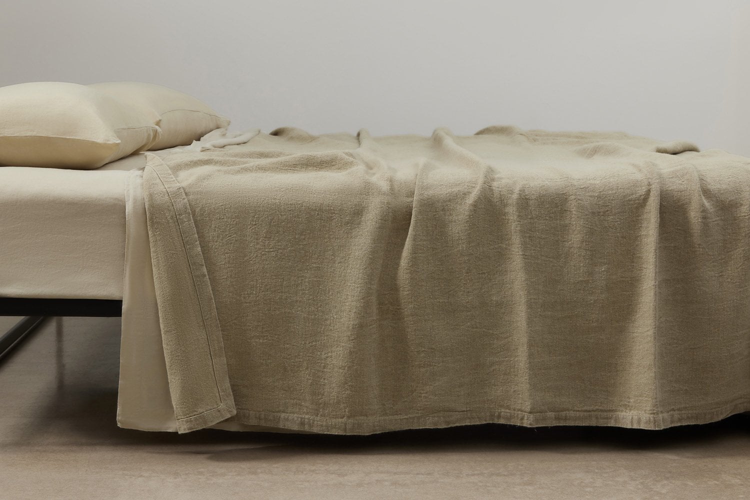 Natural fibre blanket draped over a bed in a warm, minimal living space