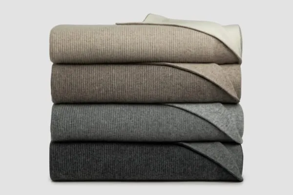 Stack of reversible Angora and Merino wool reversible rib blankets in soft neutral tones, showcasing the textured knit, contrasting colours, and luxurious natural fibres. 