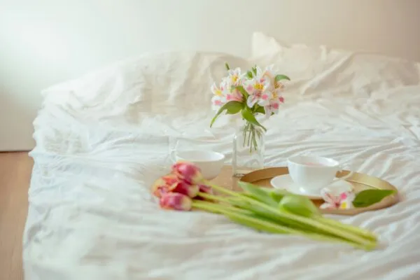 Light, breathable bedding styled with fresh flowers and breakfast on a sunlit bed.
